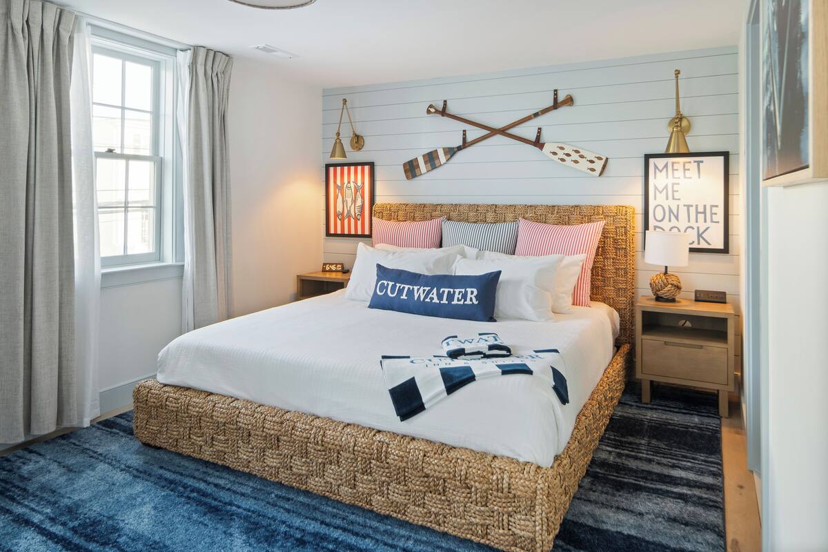 A neatly made bed with a blue pillow labeled "CUTWATER," a headboard with a striped pattern, and a wall-mounted lamp.