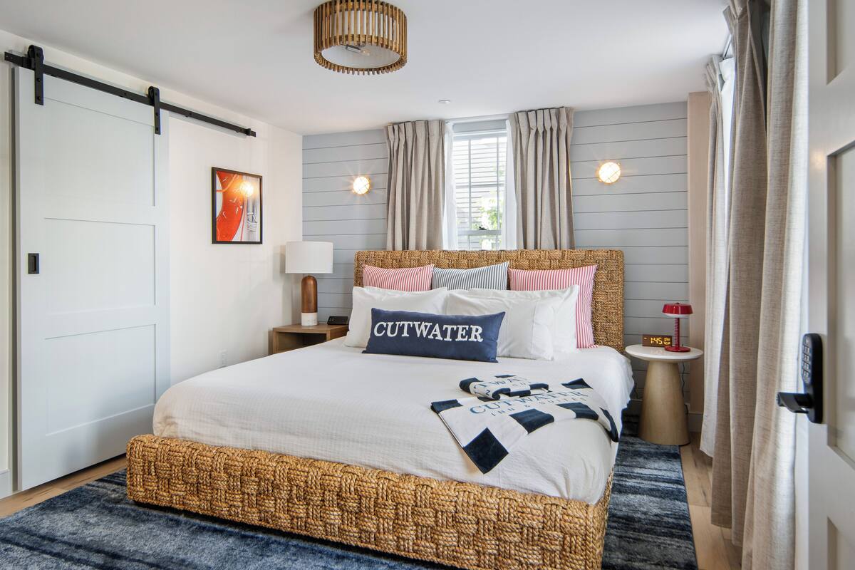 A bedroom with a bed, a bedside table with a lamp, a clock, and a window with curtains.