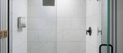 A modern shower area with white marble tiles, a glass door, and a towel rack.