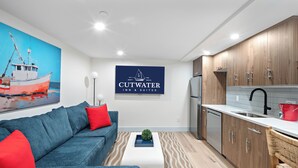 A modern kitchen with wooden cabinets, a built-in dishwasher, and a red bucket on the counter. - Cutwater Inn & Suites (Newburyport)