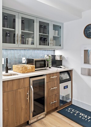 A modern kitchen with a microwave, toaster, and coffee maker on the counter, a basket, and a dishwasher. - Cutwater Inn & Suites (Newburyport)