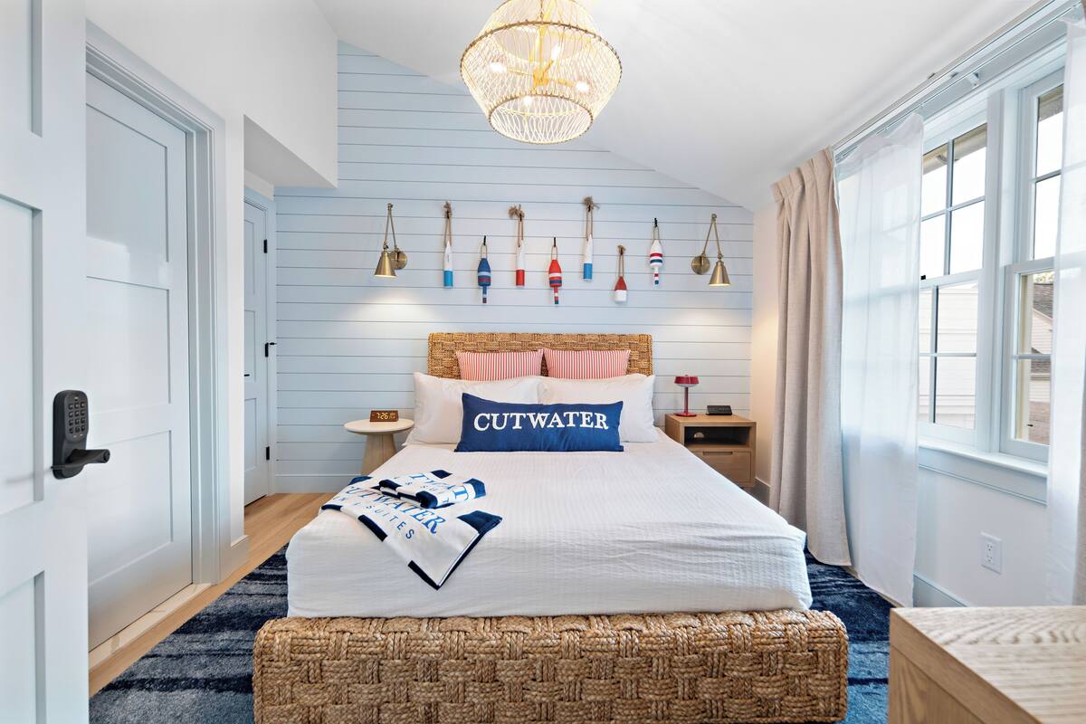 A bedroom with a bed, a bedside table, a wall-mounted lamp, a window with curtains, and a wall with nautical-themed decorations.