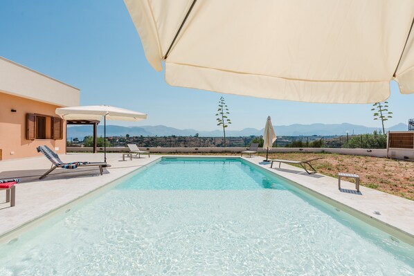 A rooftop pool with clear blue water, surrounded by lounge chairs and umbrellas, with a view of distant mountains.