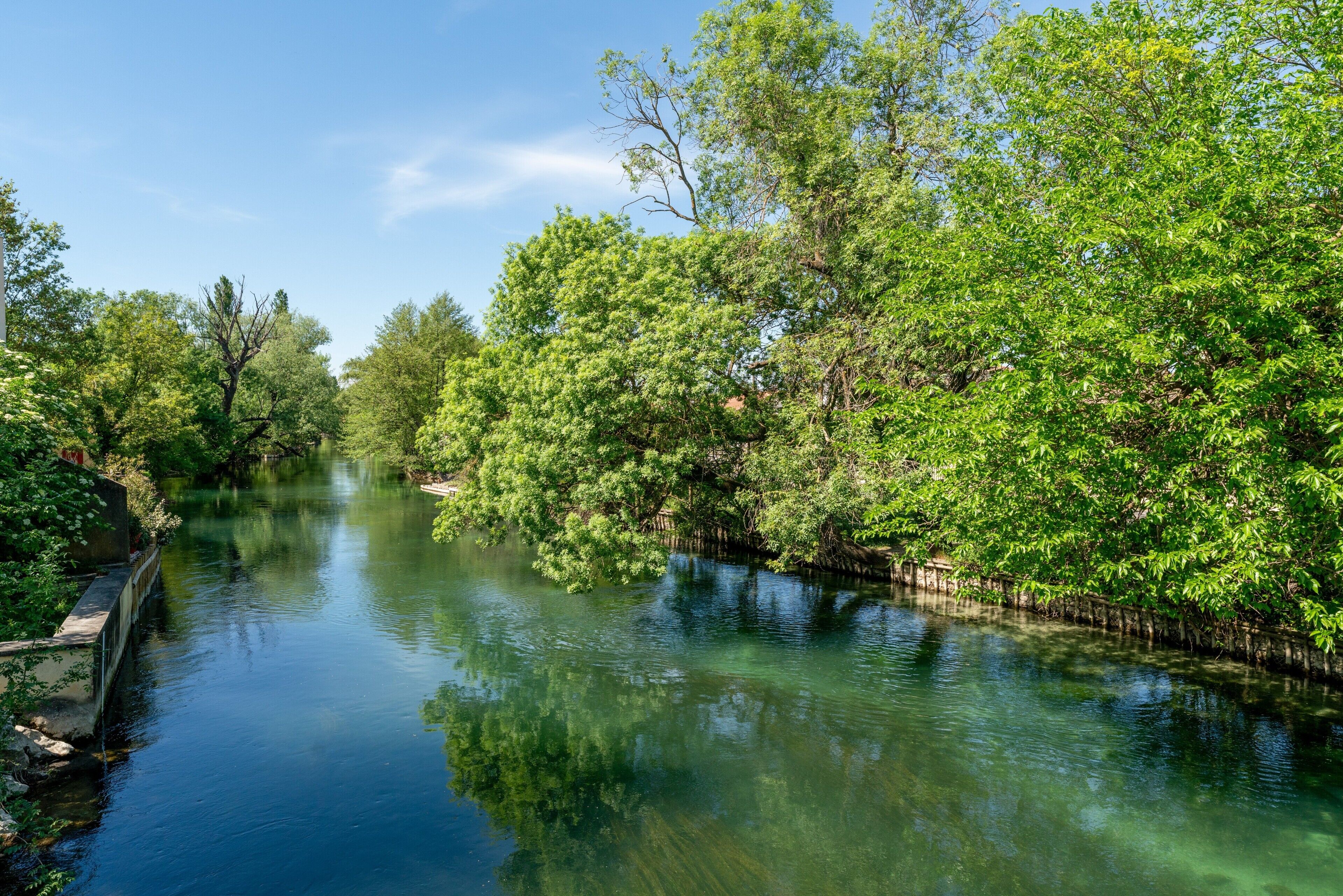 Un río tranquilo con abundante vegetación a ambos lados, cielo despejado y un puente de piedra.