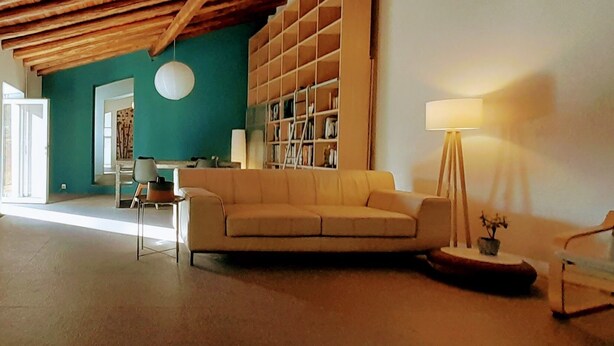 En stue med en beige sofa, træloft, bogreol og gulvlampe.