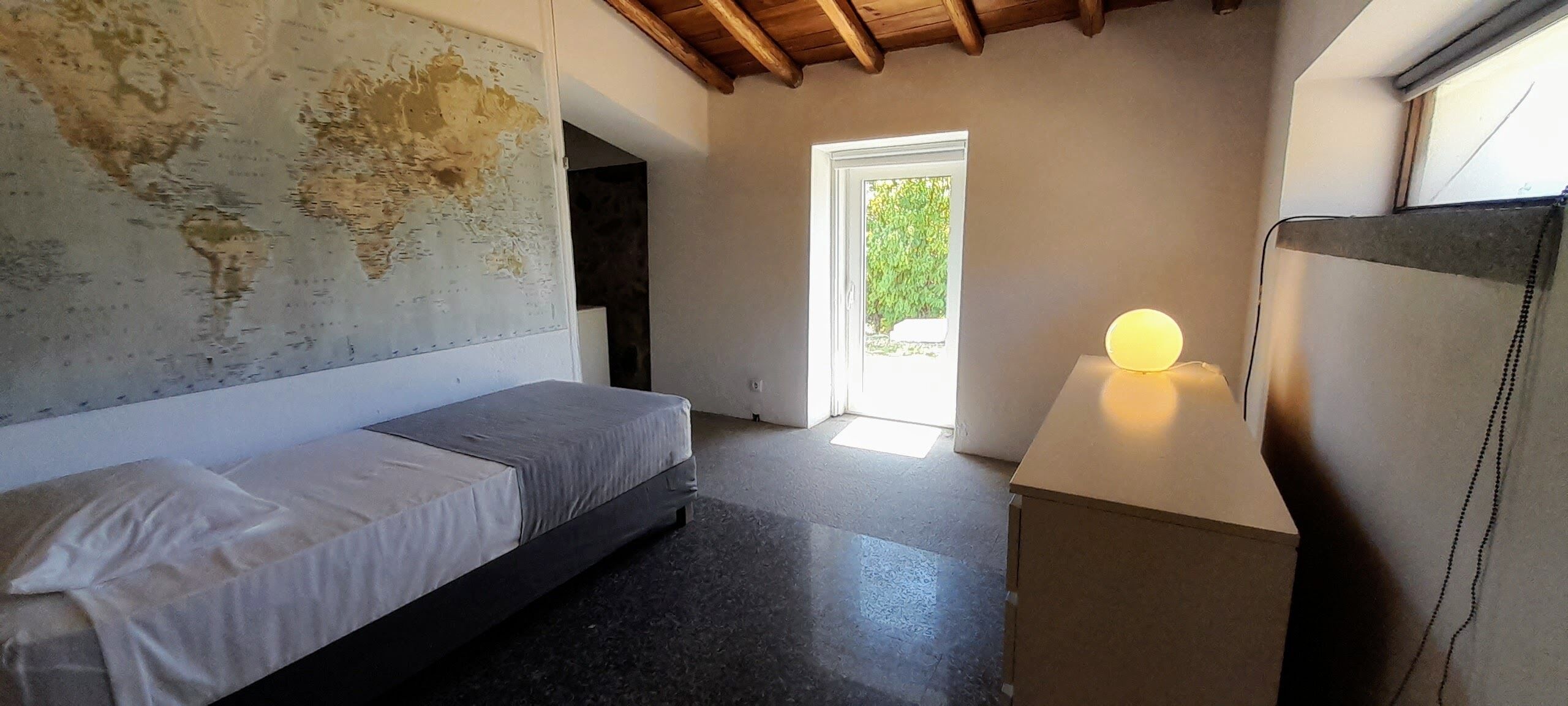 A bedroom with a bed, a map on the wall, a window, and a bedside lamp.