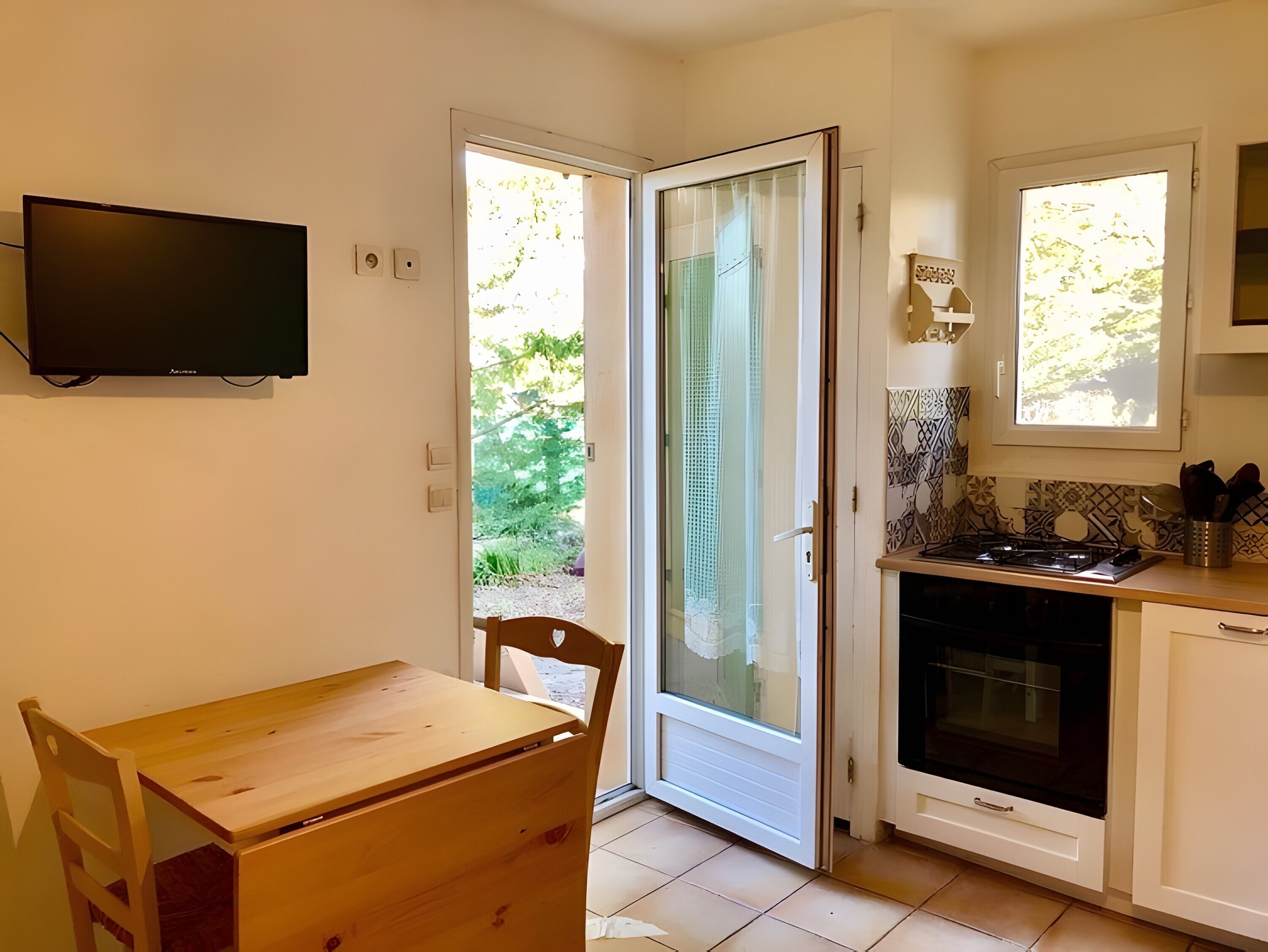 Eine kompakte Küche mit Essbereich, einem an der Wand befestigten Fernseher und einem Fenster mit Blick auf Grünflächen.