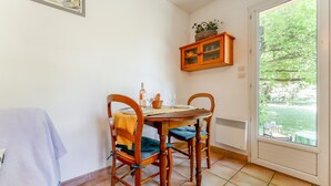 Un coin repas avec une table dressée pour quatre personnes, des chaises, un meuble placé au-dessus de la table et une vue à travers une porte vitrée.