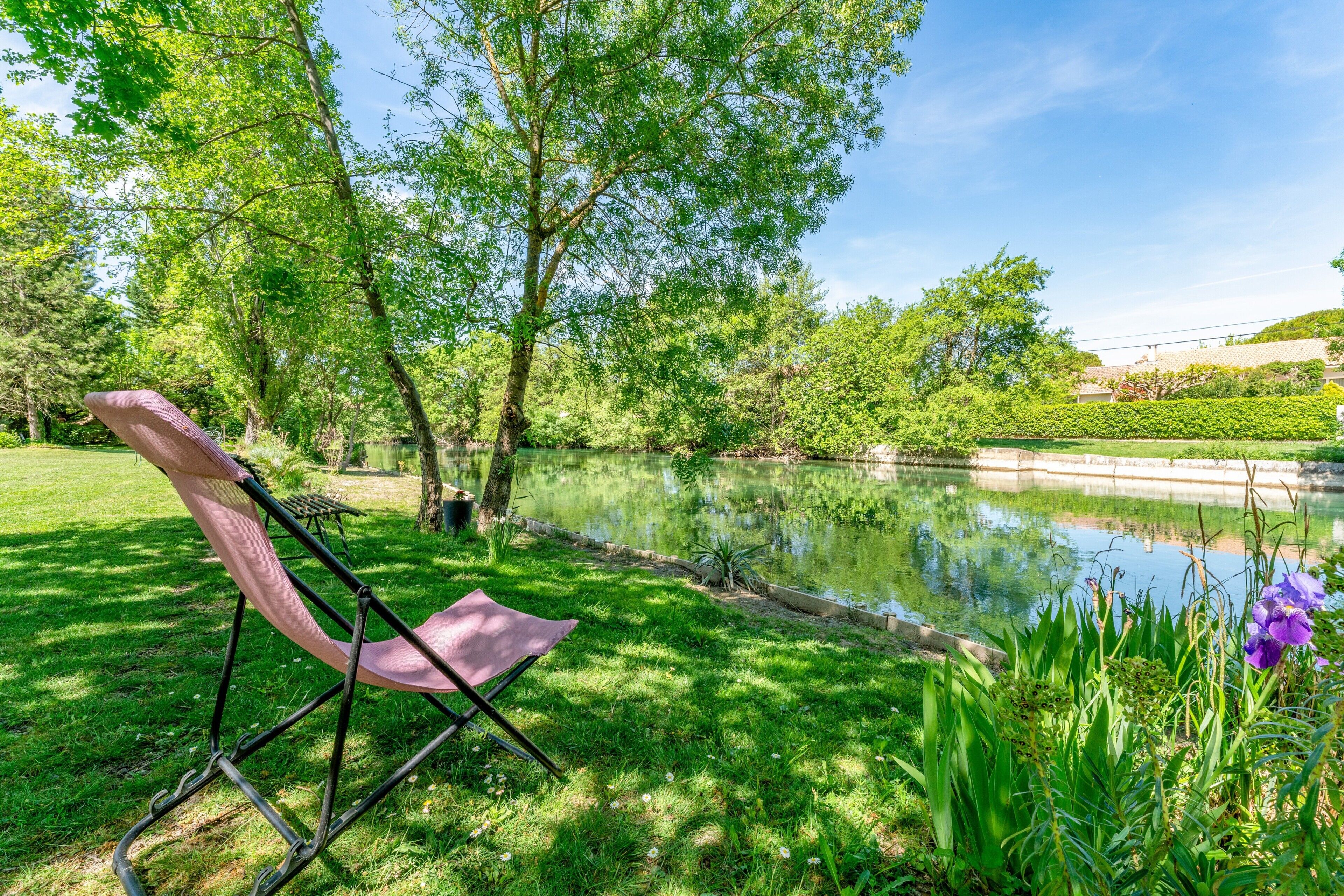 A park with a pond, greenery, and a folding chair.