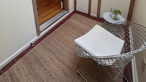 Un pasillo con una puerta que da a una cocina, una mesita con una planta y una cesta de mimbre.