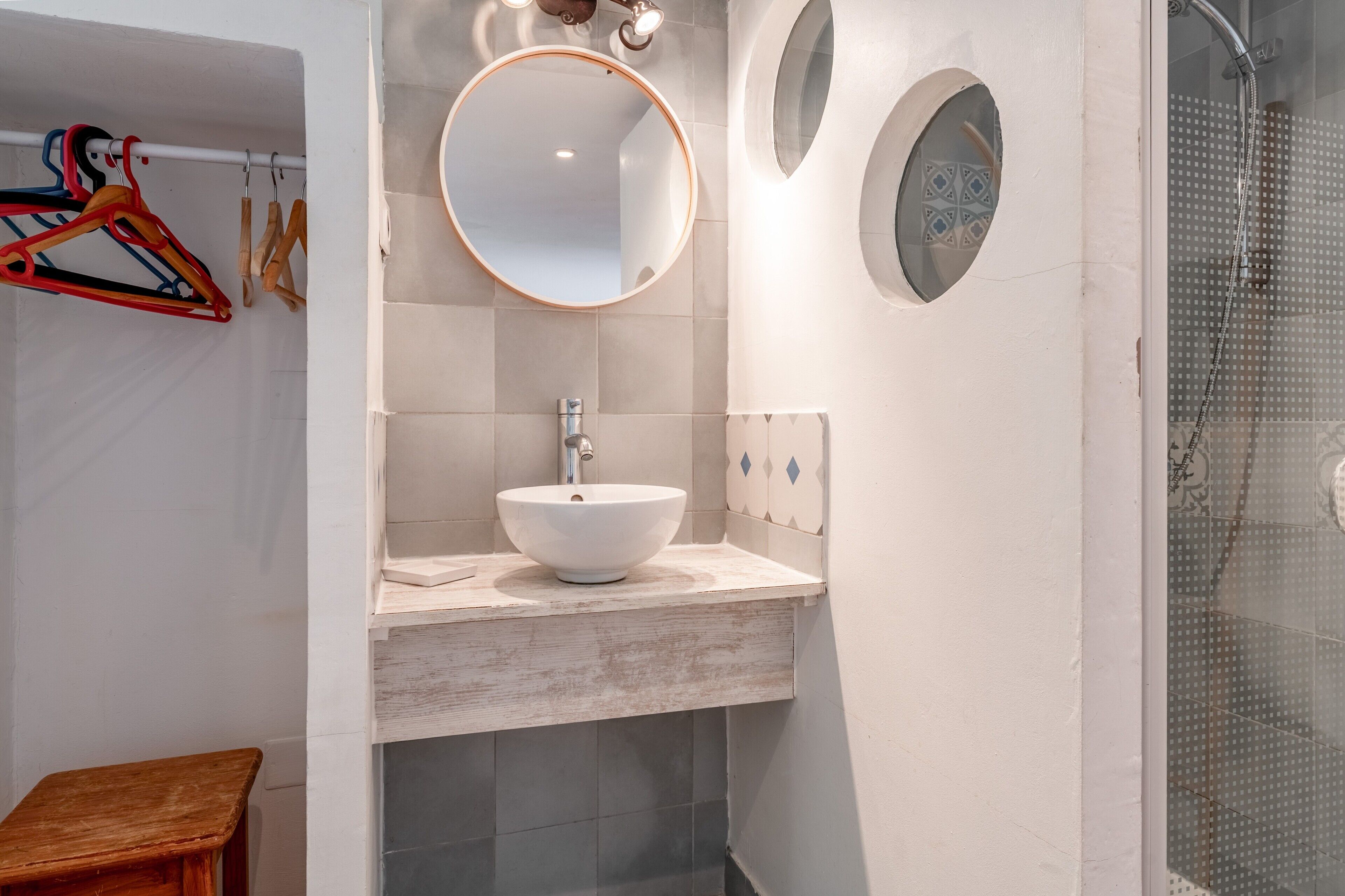 A modern bathroom with a white sink, a round mirror, and a shower.