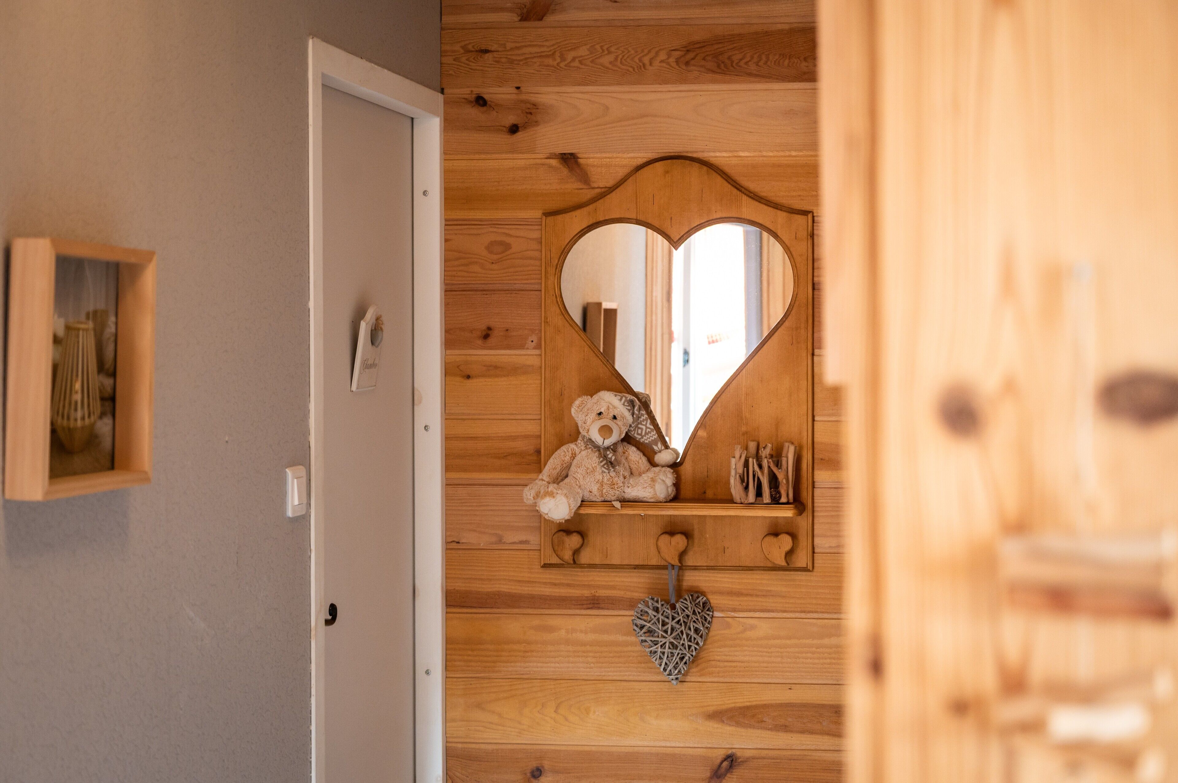 A wooden wall with a heart-shaped mirror, a teddy bear, and a heart-shaped decoration.