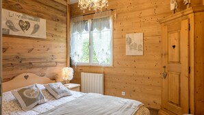 Ein Zimmer mit Holzboden, einem Bett, einer Kristalllüster und einem Kleiderschrank, sowie einem Fenster mit Vorhängen.