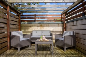 Un espace extérieur aménagé avec des meubles en osier et une table, situé sous une pergola en bois illuminée de guirlandes lumineuses.