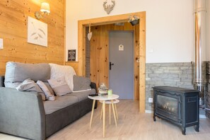 Une pièce chaleureuse avec un canapé, une petite table ronde, un poêle à bois et une porte donnant sur une autre pièce.