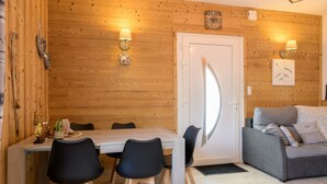Ein Zimmer mit Holzvertäfelung, einem Esstisch, Stühlen, einer Couch und Wandleuchten.