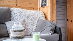 Ein gemütliches Zimmer mit einer Holzvertäfelung, einem grauen Sofa und einem kleinen runden Tisch mit einem Glas und einer grünen Kerze.