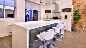 A modern kitchen with a central island, bar stools, pendant lighting, and a brick accent wall. - Exquisite condo in lovely Old Montréal with private terrace (Montréal)