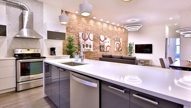 A modern kitchen with a central island, stainless steel appliances, and a brick accent wall. - Exquisite condo in lovely Old Montréal with private terrace (Montréal)