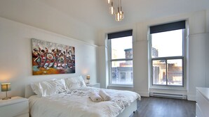 A modern bedroom with a large bed, two bedside tables, a painting, and large windows. - Exquisite condo in lovely Old Montréal with private terrace (Montréal)
