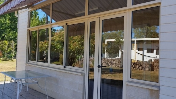 A covered patio with a glass door and windows, a metal table, and a brick wall. - Quiet house near the lake, ideal for families (Sanguinet)