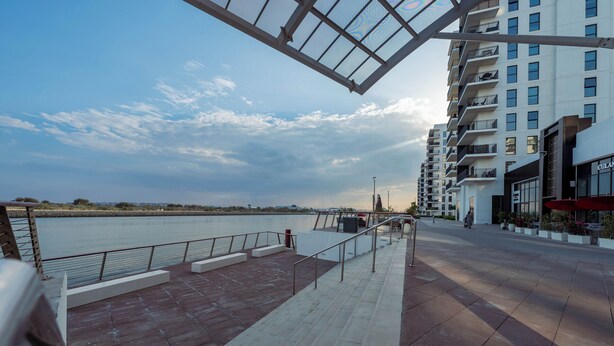 A waterfront promenade with a modern building featuring balconies and a restaurant. - Maison Privee – Chic Yas Island Escape w/ Iconic Ferrari World Vws (Abu Dhabi)