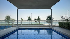 A swimming pool with a tiled edge, a covered area, and a view of a body of water and distant buildings. - Maison Privee – Chic Yas Island Escape w/ Iconic Ferrari World Vws (Abu Dhabi)