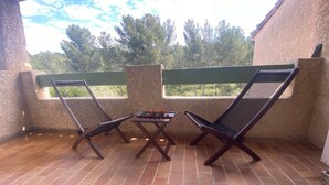 A patio with two wooden lounge chairs and a small table, a tiled floor, and a view of trees through a window. - Top: Detached Villa for 8 People • Air Conditioning • Terrace • Beaches within a 10-minute walk (Saint-Cyr-sur-Mer)