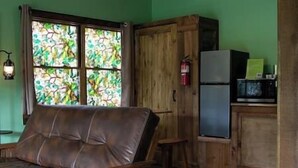 Habitació amb sofà, un armari de fusta, un frigorífic i una finestra amb vitralls.