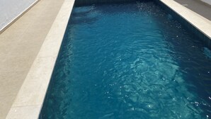A rectangular swimming pool with clear blue water, surrounded by white walls and a tiled deck. There are two lounge chairs and a black umbrella on the deck. - House with private pool close to town center (Houmet souk)