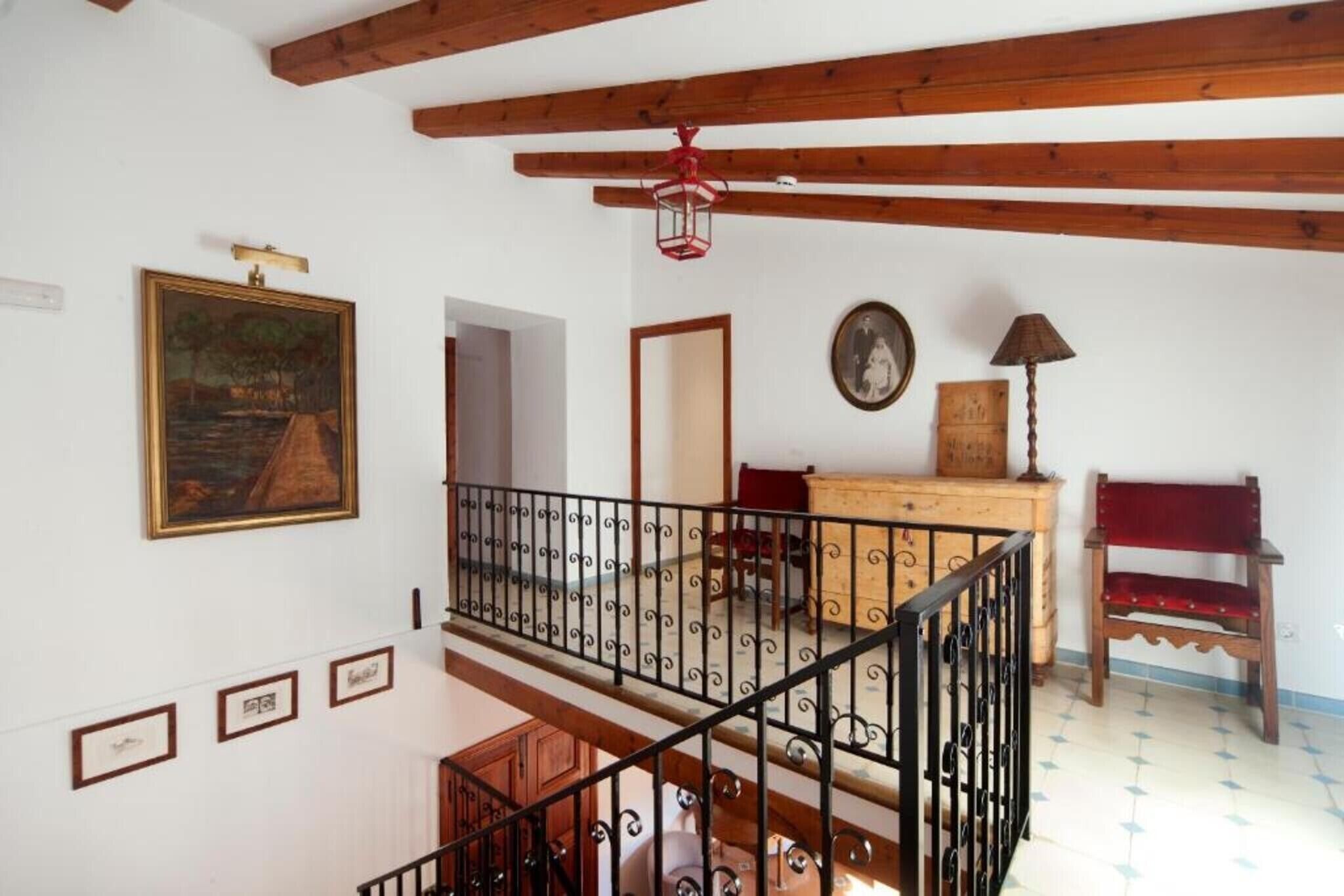 A room with a wooden staircase, a painting, a mirror, a lamp, and a red chair.