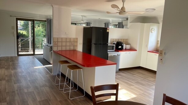 Eine moderne Küche mit roter Arbeitsplatte, einem schwarzen Kühlschrank und einem Essbereich mit einem Holzbstuhl.
