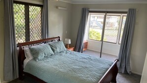 Ein Schlafzimmer mit einem Bett, einem Nachttisch, einem Fenster mit Vorhängen und Blick ins Freie.