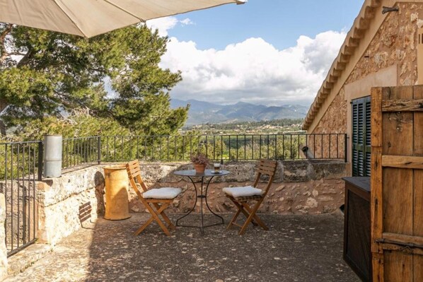 Un patio al aire libre con una mesa, sillas, un barril de madera y vistas a las montañas.