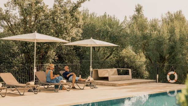 Piscina con sillas de descanso y sombrillas, rodeada de árboles.