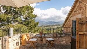 Eine Terrasse im Freien mit Tisch und Stühlen, einem Holzfass und Blick auf Berge.