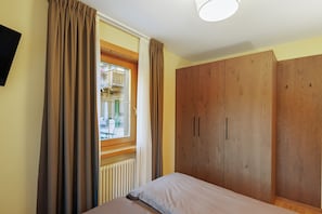 Un dormitorio con cama, armario de madera y ventana con cortinas.