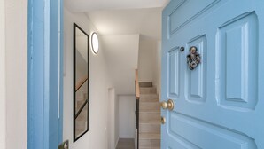 Ein Flur mit einer blauen Tür, einer Treppe und einem gerahmten Spiegel an der Wand.