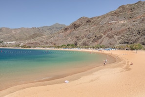 Una playa con agua cristalina, orilla arenosa y montañas al fondo.