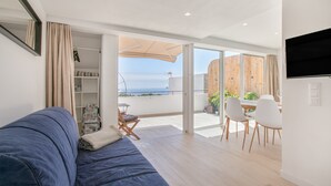 Ein modernes Wohnzimmer mit Sofa, Essbereich mit Stühlen, einem an der Wand befestigten Fernseher und einem Balkon mit Blick.