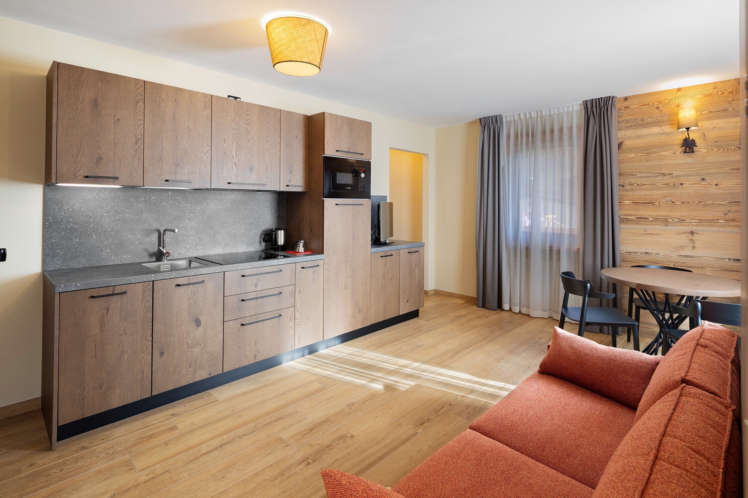 A modern kitchen with wooden cabinets, a microwave, and a sink. There is a dining area with a table and chairs.