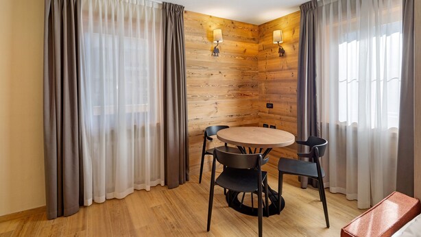 A room with a wooden wall, a round table with chairs, and curtains.