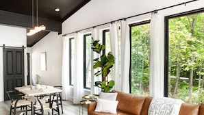 A modern living room with a brown leather sofa, a round coffee table, and a dining area with a wooden table and chairs. - The Little Timber: Cozy, Hot Tub & Fireplace! (Townsend)