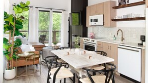 A modern kitchen with a dining area, featuring a large table, wooden flooring, and a hanging light fixture. - The Little Timber: Cozy, Hot Tub & Fireplace! (Townsend)
