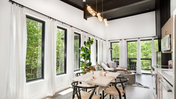 A modern kitchen with white cabinets, a large island, and a dining area with a table and chairs. - The Little Timber: Cozy, Hot Tub & Fireplace! (Townsend)