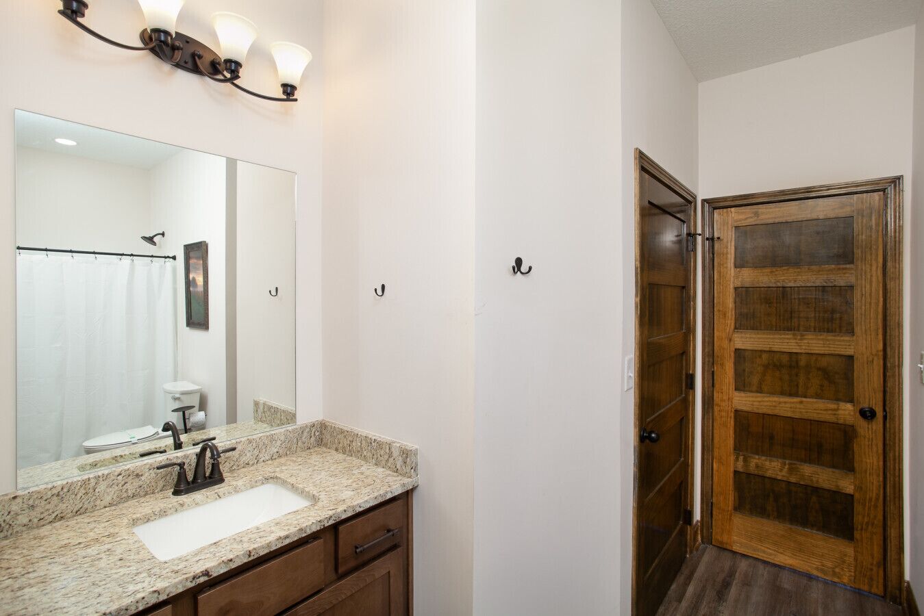 A bathroom with a granite countertop sink, a mirror, and a wooden door with glass panels.
