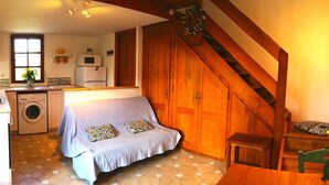 A compact kitchen with a washing machine, a sofa, and a wooden staircase.
