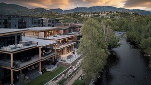 Un edifici modern d'àmbit vertical amb zones d'esbarjo a l'exterior, un riu i un paisatge de muntanyes al fons.