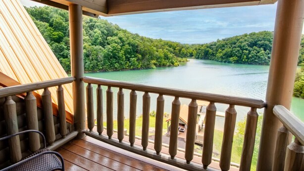 Una terraza de madera con barandilla que da a un lago rodeado de bosque.