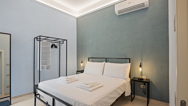 A modern bedroom with a bed, bedside tables, a hanging rack, and an air conditioning unit.